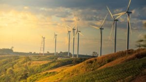 A shot of wind energy mills with green hills and the skyline in the background.